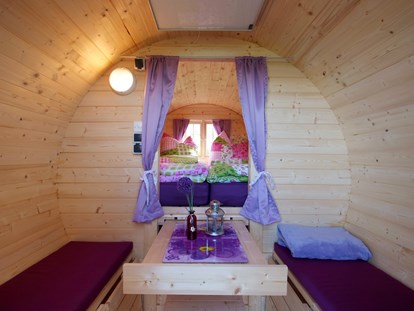 Luxury camping - Heizung - Lower Saxony - Camping-Schlaffass Innenansicht. Die Schlaffässer sind mit hochwertigen Matratzen, Kissen und Bettdecken ausgestattet. Optional kann Bettwäsche gegen Gebühr dazugebucht werden. Als weitere Ausstattung, besitzen die Fässer eine Heizung, Beleuchtung und je drei Stromanschlüsse. Unter dem einfahrbaren Tisch befindet sich ein großer Stauraum mit reichlich Platz für allerhand Gepäck. In dem Stauraum befindet sich auch eine Kiste mit Frühstücksgeschirr und eine Rollmatratze für das Kinderbett. Ein Frühstück kann optional am Kiosk dazugebucht werden. - Freizeitpark "Am Emsdeich" Schlaffass mit Seeblick auf dem Freizeitpark "Am Emsdeich"