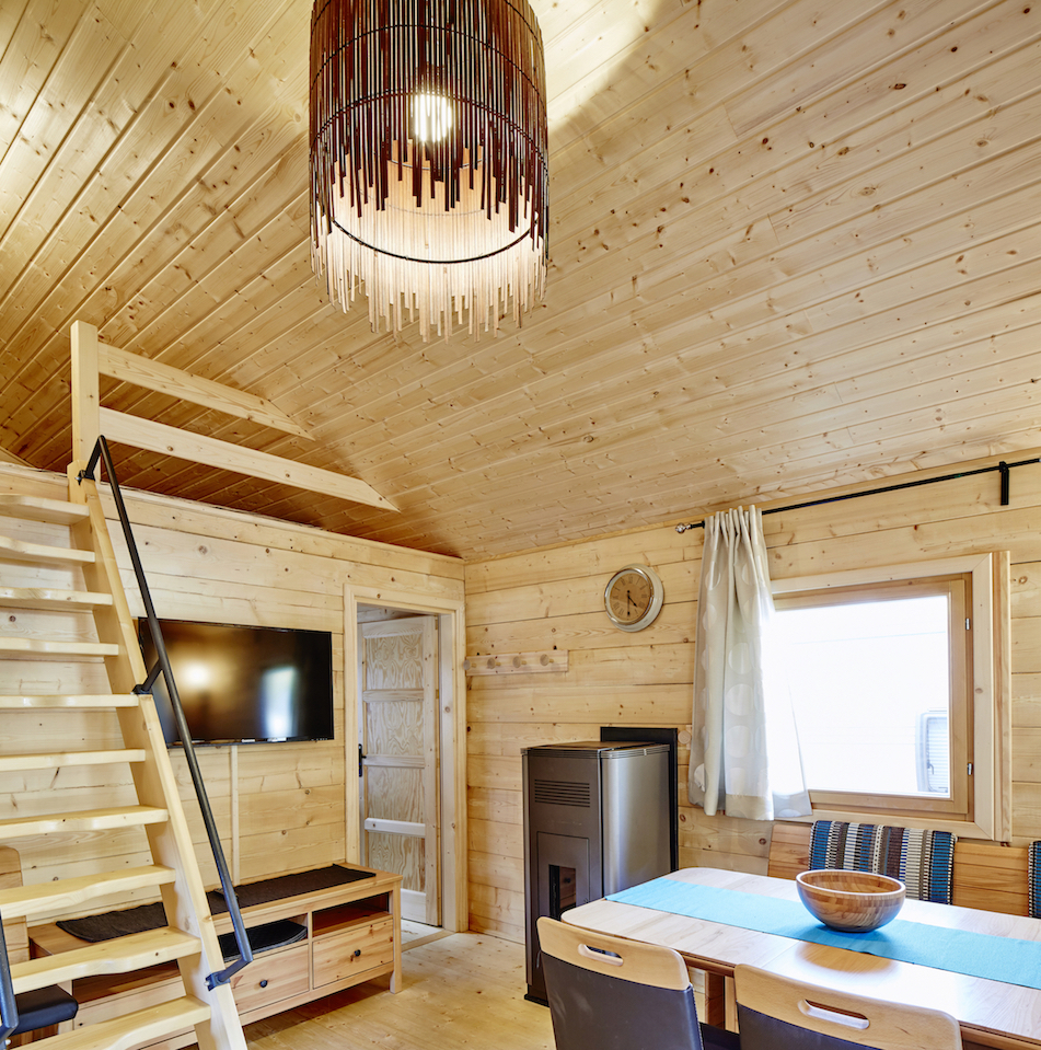 Luxuscamping: Wohnbereich mit Aufgang zum Schlafboden bzw. Relaxlounge, gemütliche Sitzecke mit Blick zum Flat-TV, Pelletsofen - Camping Dreiländereck in Tirol: Blockhütte Bergzauber Camping Dreiländereck Tirol