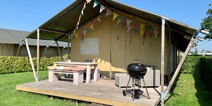 Luxuscamping - Terrasse - Süd Zeeland - Die geräumige M-Lodge mit ihrer Veranda aus Gerüstholz, der Küche und dem Lounge-Bereich ist der Macho unter den Häusern. Aber lassen Sie sich nicht von seinem robusten Äußeren täuschen; mit weichen Boxspringbetten, Lounge-Kissen und einem gemütlichen Familiengrundstück ist es cooler Typ. - Camping De Molenhoek Safari Zelt auf Camping De Molenhoek