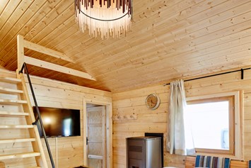 Glampingunterkunft: Wohnbereich mit Aufgang zum Schlafboden bzw. Relaxlounge, gemütliche Sitzecke mit Blick zum Flat-TV, Pelletsofen - Blockhütte Bergzauber Camping Dreiländereck Tirol
