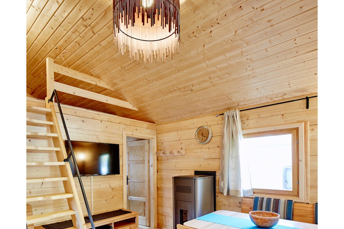 Glampingunterkunft: Wohnbereich mit Aufgang zum Schlafboden bzw. Relaxlounge, gemütliche Sitzecke mit Blick zum Flat-TV, Pelletsofen - Blockhütte Bergzauber Camping Dreiländereck Tirol