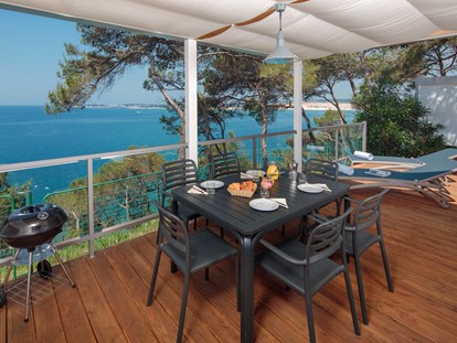 Luxury camping - große und überdachte Terrasse mit einem Außensofa, Liegestühlen und einem wunderschönen Meerblick - Mobilheim Premium Vista Mare auf Lanterna Premium Camping Resort