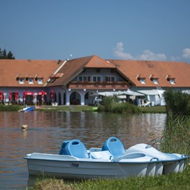Glamping: Außenansicht Pension und Seerestaurant Pirkdorfer See mit dem Pirkdorfer See im Vordergrund. - Lakeside Petzen Glamping Resort