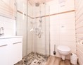 Glamping: Badezimmer im Ferienhäuschen mit bodentiefer Regendusche, WC und Spiegelschrank.  - Ostseecamping Ferienpark Zierow