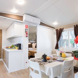 Glampingunterkunft: Wohnzimmer mit Küche und im unteren Schlafzimmer der Kinder - Mobilheim Top Residence Platinum auf Camping Vela Blu