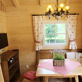 Glampingunterkunft: Ferienhütte "Drachenwand": gemütliche Sitzecke mit Fernseher (SAT-Anlage) und Aufgang zur Galerie mit Schlafmöglichkeit - Ferienhütten am CAMP MondSeeLand