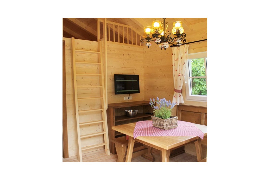 Glampingunterkunft: Ferienhütte "Schafberg": gemütliche Sitzecke mit Fernseher (SAT-Anlage) und Aufgang zur Galerie mit Schlafmöglichkeit - Ferienhütten am CAMP MondSeeLand